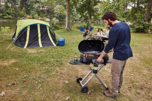 Man grilling food at a campsite with family in the background